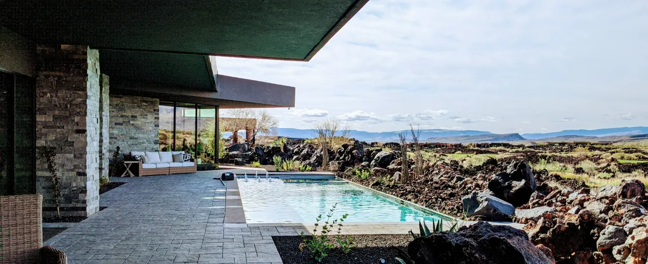 Clear pool beside a covered patio and volcanic rock landscape